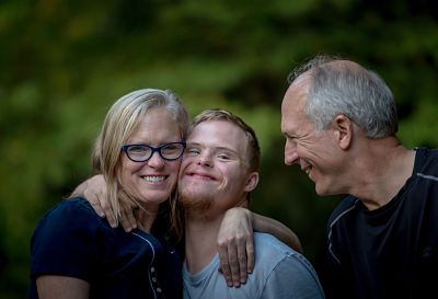 Woman smiling with arm around one younger man, older man smiling at them